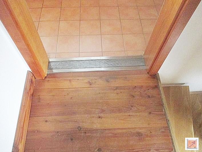 Fachgerechte Materialtrennung: Fliesenboden trifft auf Douglasie-Holzriemen. Edelstahlrinne als Übergang zwischen Badfliesen und massiven Douglasie-Holzdielen im Holzhaus.